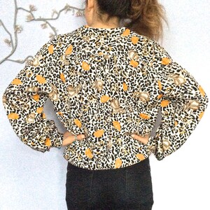 May include: A white blouse with a leopard print and orange floral accents. The blouse has long sleeves and a gathered neckline.