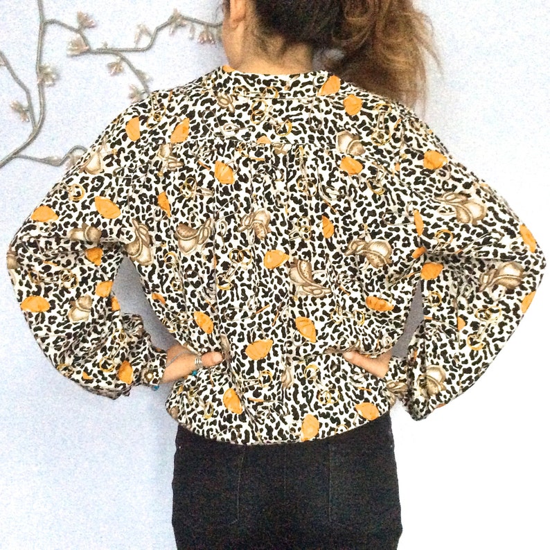 May include: A white blouse with a leopard print and orange floral accents. The blouse has long sleeves and a gathered neckline.