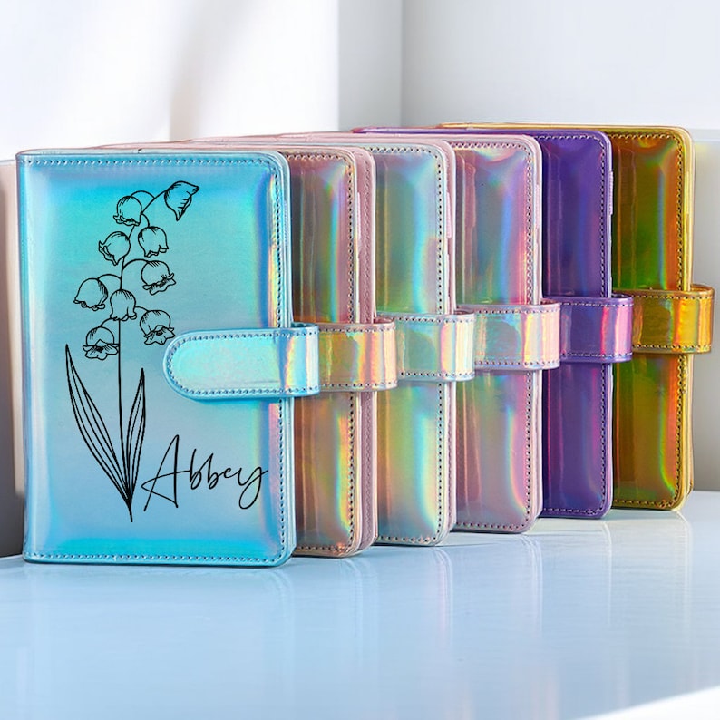 May include: Five iridescent rainbow-colored binders with a floral design and the name "Abbey" on the front.