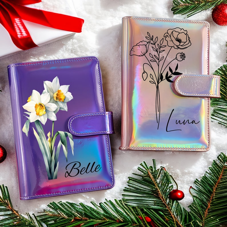 May include: Two iridescent purple and pink personalized journals with floral designs. The purple journal has a daffodil design and the text "Belle" on the front. The pink journal has a poppy design and the text "Luna" on the front.
