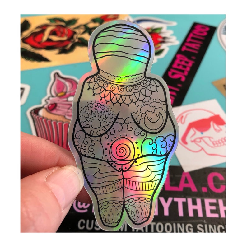 Puede incluir: Una pegatina hologr&aacute;fica de una figura femenina con intrincados patrones y un dise&ntilde;o en espiral en el centro. La pegatina tiene un acabado iridiscente arco&iacute;ris.