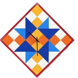May include: A diamond-shaped wall clock featuring a geometric quilt-inspired pattern in shades of blue, orange, yellow, and white. The clock has a thin red frame and three black hands centred on the face, which displays a repeating star motif.