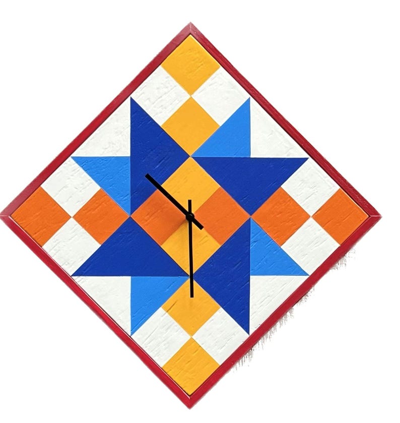 May include: A diamond-shaped wall clock featuring a geometric quilt-inspired pattern in shades of blue, orange, yellow, and white. The clock has a thin red frame and three black hands centred on the face, which displays a repeating star motif.