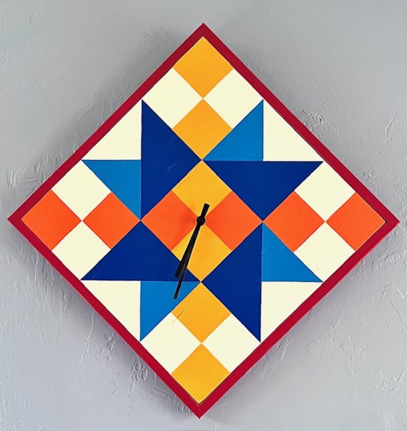 May include: A diamond-shaped wall clock featuring a geometric star pattern in shades of blue, orange, yellow, and cream. The clock has a thin red border and two black hands positioned in the centre. The design is composed of various triangles and squares.