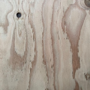 May include: A light-coloured plywood sheet featuring a natural wood grain pattern with visible vertical streaks in shades of tan and beige. The surface displays several dark circular knots of varying sizes scattered across the textured wooden panel.