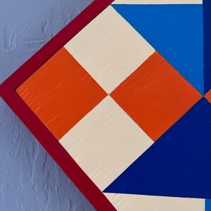 Detail of Spinning Star Barn Quilt Block in orange and blue geometrics on a white background.