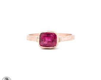 May include: A delicate ring with a hammered rose gold band and a vibrant pink gemstone set in a square bezel.