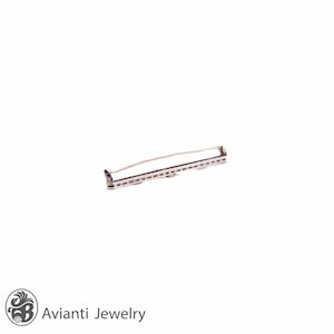May include: A silver-toned brooch with a geometric design. The brooch has a long, rectangular shape with a row of small, round stones set in the center.