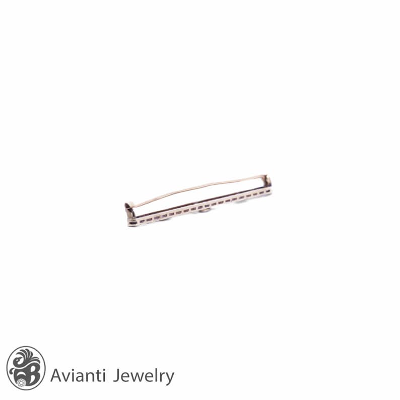 May include: A silver-toned brooch with a geometric design. The brooch has a long, rectangular shape with a row of small, round stones set in the center.