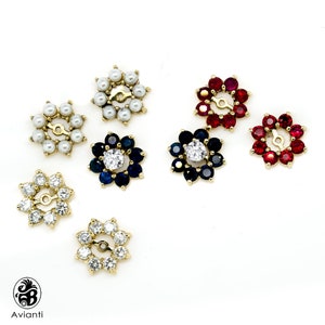 May include: Six gold flower-shaped earring charms with different coloured gemstones. The charms feature a centre stone surrounded by smaller stones. The stones are white pearls, red rubies, blue sapphires, and clear diamonds.