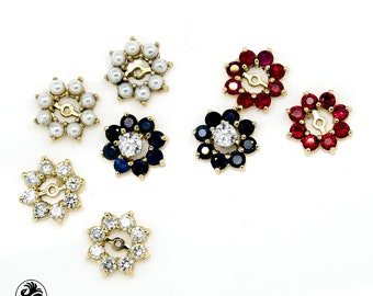 May include: Six gold flower-shaped earring charms with different colored gemstones. The charms feature a center stone surrounded by smaller stones. The stones are white pearls, red rubies, blue sapphires, and clear diamonds.