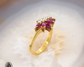 Op de afbeelding: Een gouden ring met een cluster van roze robijnen en witte diamanten, gezet in een bloemvormig ontwerp.