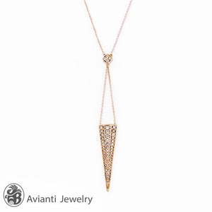 May include: A delicate gold necklace with a diamond-encrusted pendant shaped like a triangle. The pendant hangs from a thin chain with a smaller diamond-encrusted pendant at the top.