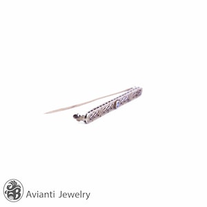 May include: A delicate silver filigree bar brooch with a single blue gemstone in the center.