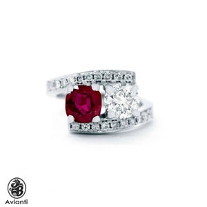 May include: A white gold ring with a vivid red ruby and a brilliant diamond. The band is set with small, clear gemstones. The ring's design is contemporary and elegant. The ring is suitable for special occasions.