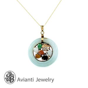 Puede incluir: Un collar dorado con un colgante circular. El colgante presenta un anillo de jade azul claro con un centro dorado. El centro tiene un pequeño diseño de casa y está rodeado de piedras preciosas de colores. El collar está sobre un fondo blanco.