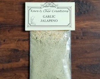 Op de afbeelding: Een klein doorzichtig plastic zakje gevuld met lichtgroen poeder. Het zakje heeft een wit label met de tekst "Kare & Cher Creations Garlic Jalapeno".