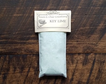 Op de afbeelding: Een witte zak met een label met de tekst "Kare & Cher Creations KEY LIME". De zak is gevuld met een lichtblauwe substantie.