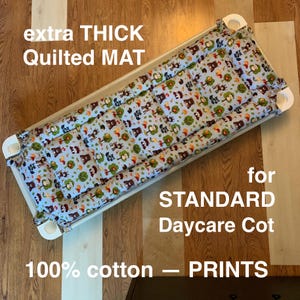 May include: An extra thick, quilted mat for a standard daycare cot. The mat features a light blue background with a repeating pattern of brown bears, green trees, and red accents. The text on the image reads "extra THICK Quilted MAT" and "100% cotton - PRINTS".