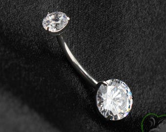 May include: A curved barbell body jewelry piece featuring a polished silver-tone metal shaft with a small clear round faceted gemstone at the top and a larger clear round faceted gemstone at the bottom, both secured in prong settings.