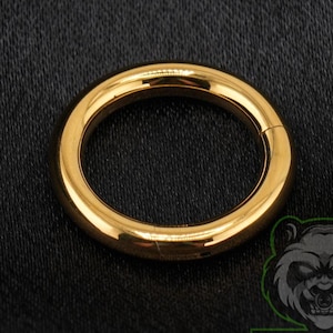 May include: A polished gold-colored circular hoop ring featuring a seamless design. The jewelry piece has a smooth, reflective metallic surface and a continuous round shape, presented with a clean, minimalist aesthetic for various body piercings.