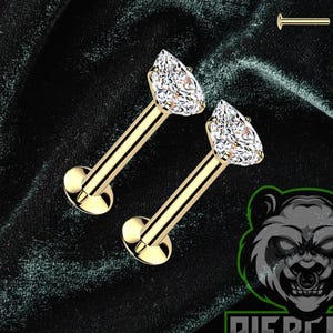 May include: Gold-coloured lip piercing studs with teardrop-shaped, clear crystal stones. The image also shows additional studs and the "Piercing Panda" logo with a panda bear graphic.