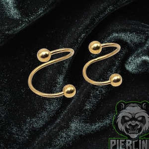 May include: A pair of gold-colored spiral earrings with a small ball at each end. The earrings are displayed on a dark green velvet surface. The logo "Piercing Panda" is visible in the bottom right corner.