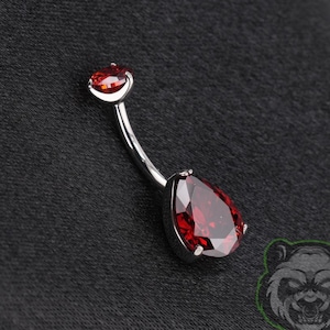 May include: A curved barbell belly button ring featuring a polished silver-tone metal shaft. The top end has a small round red gemstone, while the bottom end features a larger, teardrop-shaped red gemstone set in a silver-tone metal frame.