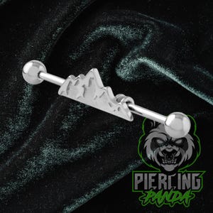 May include: A silver industrial barbell piercing with a mountain range design. The barbell has a straight bar with a ball on each end and a mountain-shaped charm in the center. The piercing is made of shiny metal.