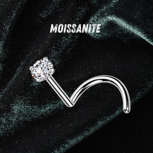 May include: A silver-toned nose stud featuring a round, faceted moissanite gemstone in a prong setting. The metal post is curved into a spiral shape. The text MOISSANITE is printed in white above the jewelry piece.