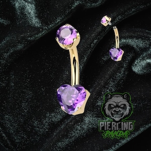 Pode incluir: Anel de umbigo dourado com uma pedra preciosa roxa em forma de coração. O anel tem uma barra curva e uma gema redonda no topo. Uma versão menor do anel também é mostrada. O logotipo "Piercing Panda" está no canto inferior direito.