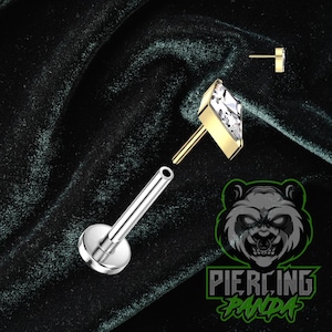 Puede incluir: Un labret de color dorado con una gema transparente de corte cuadrado y un poste plateado. La imagen también muestra un poste plateado separado y un tubo de perforación. El logotipo "Piercing Panda" es visible en la esquina inferior derecha.