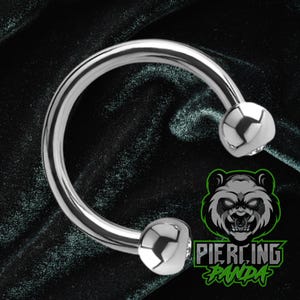 May include: A shiny, silver horseshoe barbell piercing. The curved barbell has a smooth, polished finish and is capped with two rounded, faceted ends. The background is a dark, textured fabric. The logo for Piercing Panda is in the lower right corner.