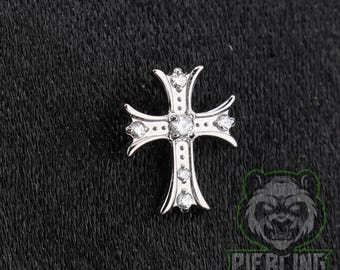 May include: A silver-toned cross-shaped jewelry piece featuring five clear, round-cut stones set into the metal. The cross has a flared design at each of the four ends, with a central stone and one stone positioned on each of the four arms of the cross.