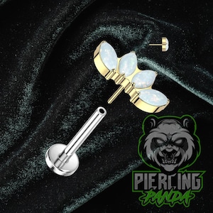 Puede incluir: Un piercing labial plateado con una base plana y un tubo hueco. El piercing está diseñado para sostener una pieza decorativa dorada con tres piedras ovaladas y opalinas. También se incluye un pequeño poste dorado.