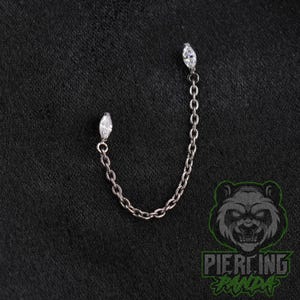May include: A silver-toned metal body jewelry piece featuring a delicate chain connecting two marquise-cut clear gemstones. The jewelry is designed with a post at each end, allowing the chain to drape between two separate piercing points.