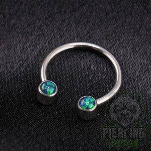 May include: A circular horseshoe-shaped body jewelry piece made of polished silver-toned metal. The two ends of the open hoop feature rounded, cabochon-style settings containing iridescent blue and green faux opal stones with a smooth finish.