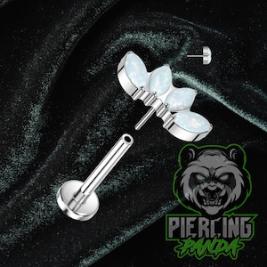 Puede incluir: Un piercing labial plateado con una parte superior decorativa con tres piedras ópalo ovaladas. El piercing está desmontado, mostrando el poste y la base roscada. La imagen está sobre un fondo verde oscuro texturizado.