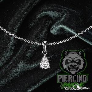 May include: A silver necklace with a pear-shaped, clear crystal pendant. The chain is delicate and the pendant is suspended from a small loop. The background is a dark green velvet.