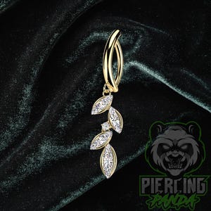 Pode incluir: Um piercing de umbigo dourado com um design de folhas penduradas. As folhas são adornadas com pedras preciosas transparentes e brilhantes. A joia é exibida em um fundo de veludo verde escuro. O logotipo Piercing Panda é visível no canto inferior direito.