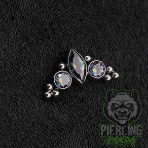 May include: A silver-toned body jewelry piece featuring a central marquise-cut iridescent stone flanked by two round iridescent stones. The design includes small metallic spheres arranged in clusters at the ends, creating a symmetrical arc shape.