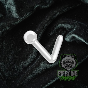 May include: Clear, L-shaped nose stud with a rounded top. The piercing is made of a transparent material and is set against a dark, textured background. The Piercing Panda logo is visible in the lower right corner.