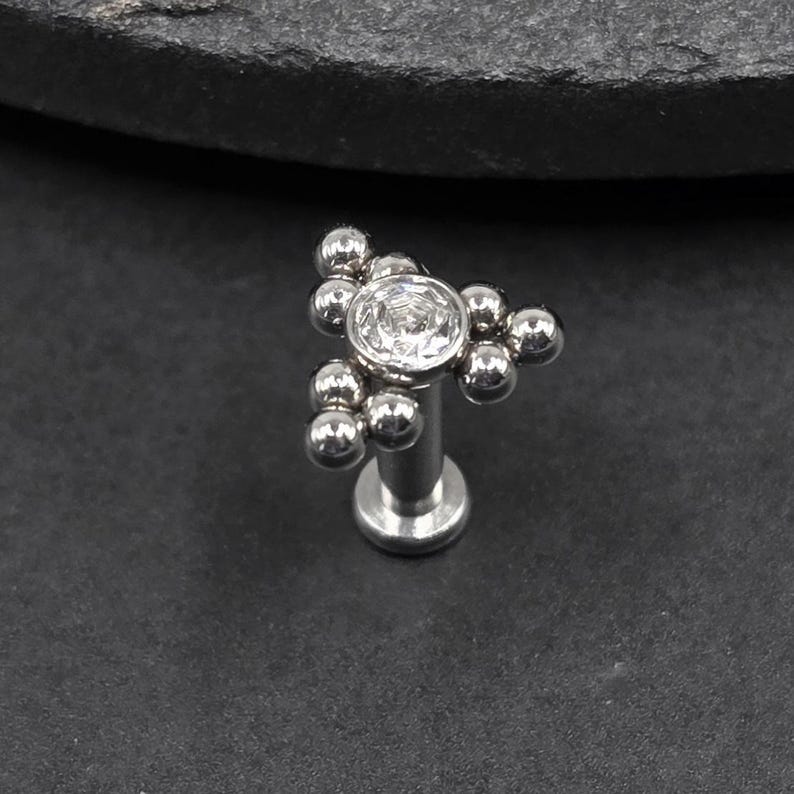 May include: Silver body jewellery with a clear gem and a cluster of small silver balls.