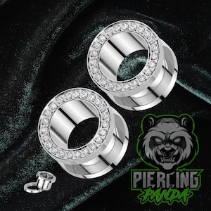 May include: Two silver-colored ear gauges with a ring of clear rhinestones around the outer edge. A smaller gauge is next to the larger ones. The image also includes a logo with a panda and the words "Piercing Panda."