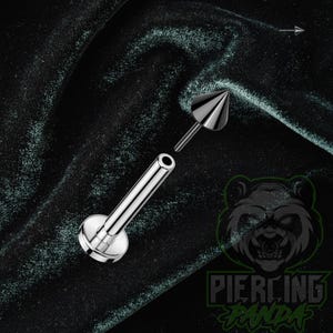 May include: A silver-colored metal labret piercing jewelry piece consisting of a flat circular base, a straight post, and a detachable cone-shaped top. The components are shown separated, with the cone top hovering above the post.