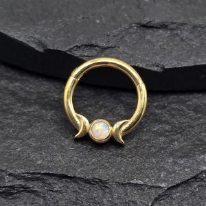 May include: Gold body jewelry with a crescent moon design and an iridescent opal gemstone.