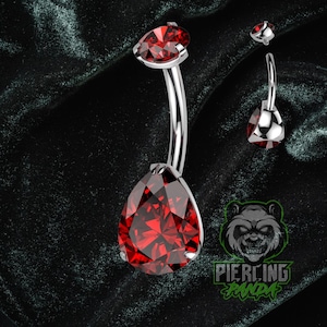 May include: A silver belly button ring with a teardrop-shaped, faceted, red gemstone. The ring has a curved barbell design with a smaller, matching gemstone at the top. The image also includes a logo with the text "Piercing Panda."