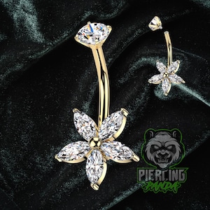 Op de afbeelding: Een goudkleurige navelpiercing met een bloemdesign. De bloem heeft zes heldere, marquise-geslepen stenen rond een centrale gouden kraal. Een kleinere, bijpassende bloem en een enkele edelsteen zijn ook zichtbaar.