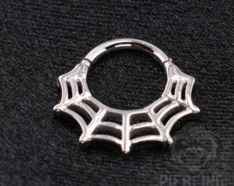 May include: A silver-toned circular segment ring featuring a decorative spider web design along the lower half. The metal jewellery piece has a polished finish and a hinged mechanism, showcasing a detailed web pattern with cut-out sections.