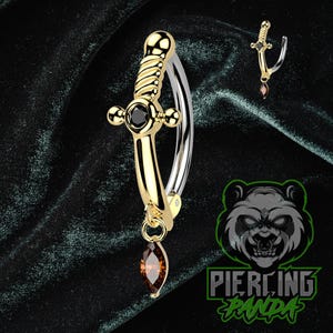 Pode incluir: Um piercing corporal de barra curva dourada com um design de adaga e uma gema marrom pendurada. A adaga apresenta uma gema preta e uma alça torcida. Uma versão menor do piercing também é visível.